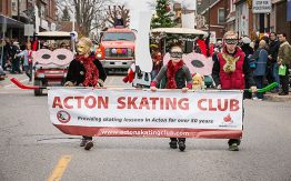 children in masks holding Acton Skating Club banner in parade