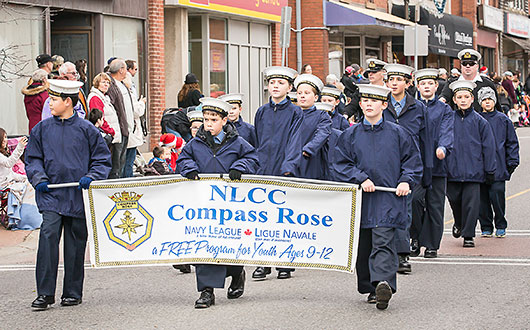 children in blue jackets and white caps holding Navy League banner in parade