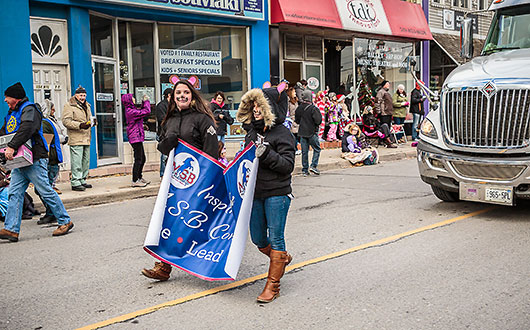two girls walking in the parade holding a banner of MacKenzie Smith Bennett school