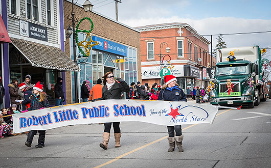 two kids and one adult holding "Robert Little Public School" banner in Santa Claus parade